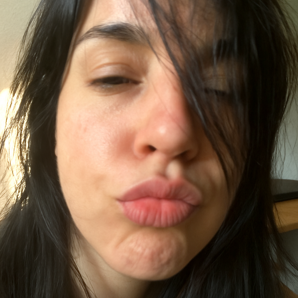 Mujer de cabello oscuro toma una selfie en primer plano, con el rostro parcialmente cubierto por mechones y los labios fruncidos en gesto de beso.