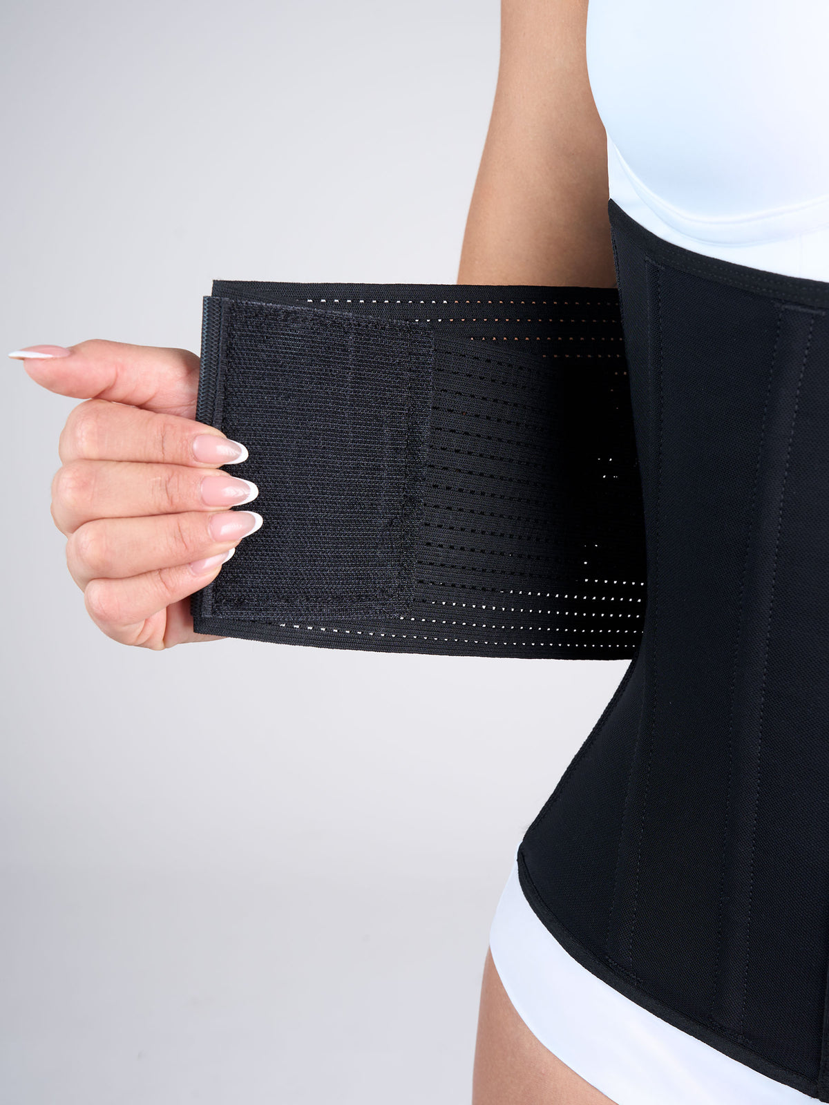 Close-up of a woman wearing the black Hourglass Waist Cincher with Elastics, Colombian shapewear with front hooks and open side elastics for a custom fit and extra compression #color_Black