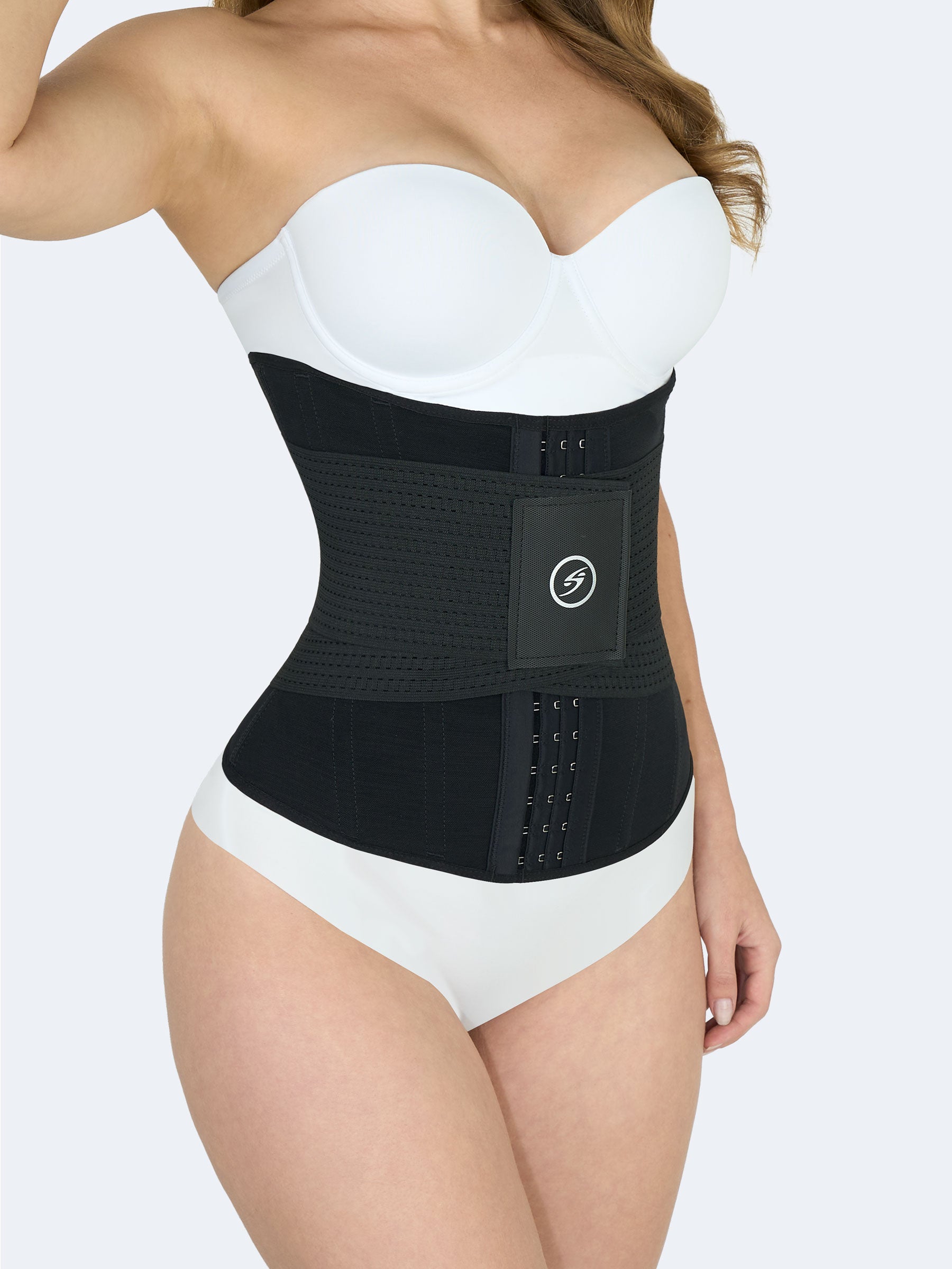 Mujer mostrando Cinturilla Reloj de Arena con Elásticos en color negro, Faja Colombiana vista lateral con broches y banda de velcro que moldea la cintura y proporciona compresión adicional #color_Black / Negro