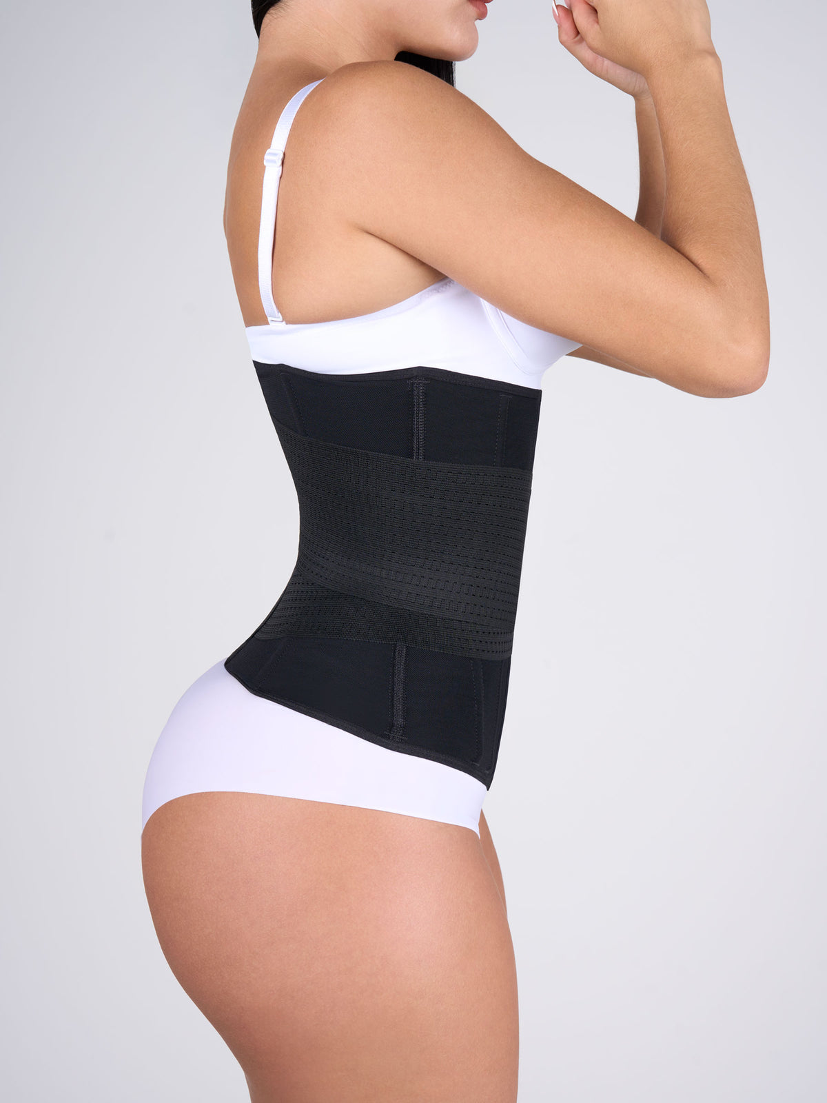 Woman showing the black Hourglass Waist Cincher with Elastics, Colombian shapewear seen from the side, with hooks and a velcro band that shapes the waist and adds compression #color_Black