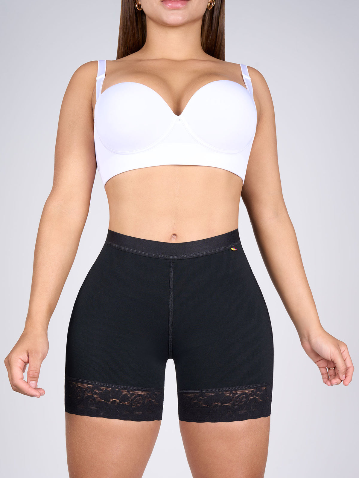 Woman showing black short butt-lifting shorts, Colombian shapewear that defines the tummy, shapes the hips and lifts the glutes with floral lace at the thighs #color_Black