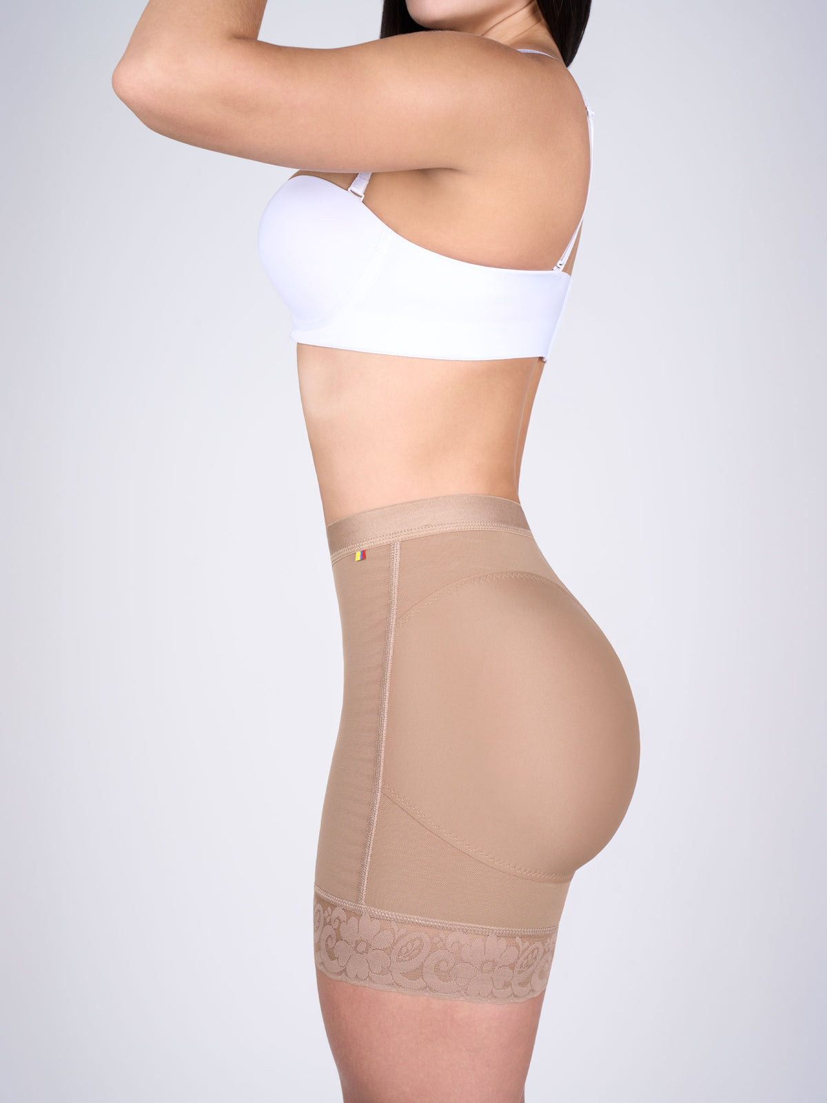 Mujer usando short levanta cola corto en color cocoa, Faja Colombiana que moldea la cintura y realza los glúteos con encaje floral en los muslos. #color_Moca