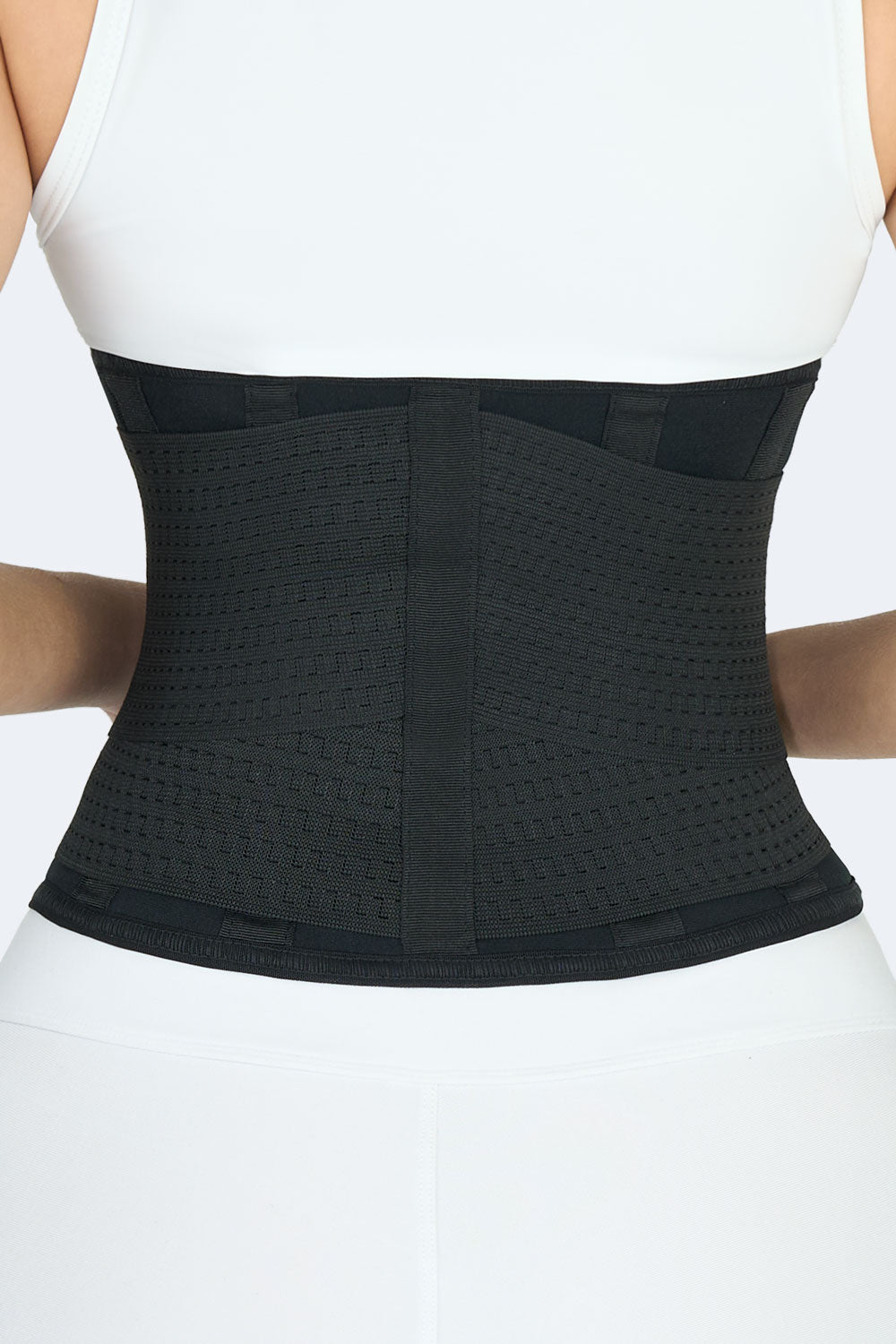 Acercamiento vista posterior de mujer con cinturon en neopreno negro, diseño ajustado con refuerzo lumbar y bandas elasticas para soporte y entrenamiento.