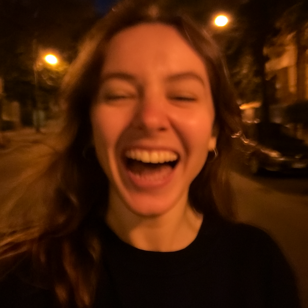 Mujer joven sonríe ampliamente en una selfie nocturna al aire libre. La imagen está un poco movida y detrás se ven luces de la calle y árboles.