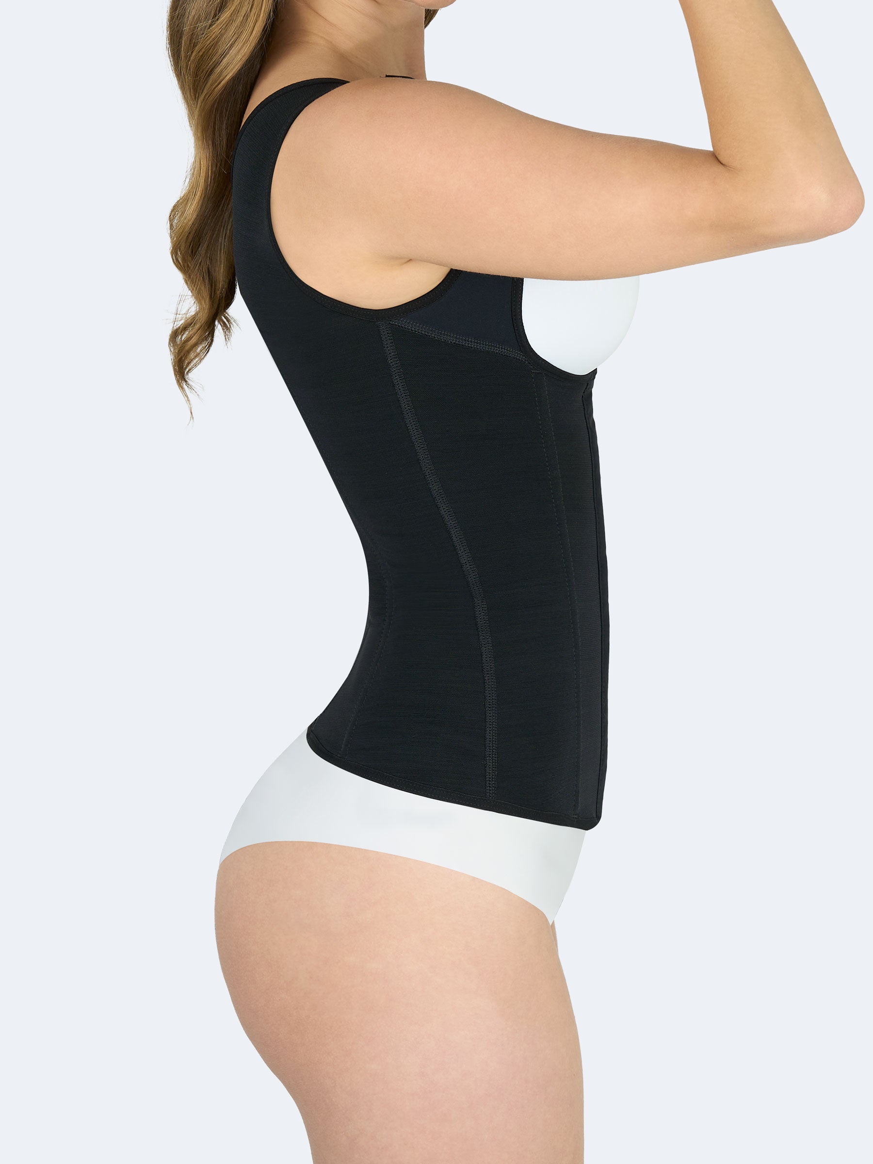 Mujer mostrando Chaleco Moldeador en color negro, Faja Colombiana vista lateral que estiliza la cintura, controla el abdomen y brinda soporte en la espalda #color_Black / Negro