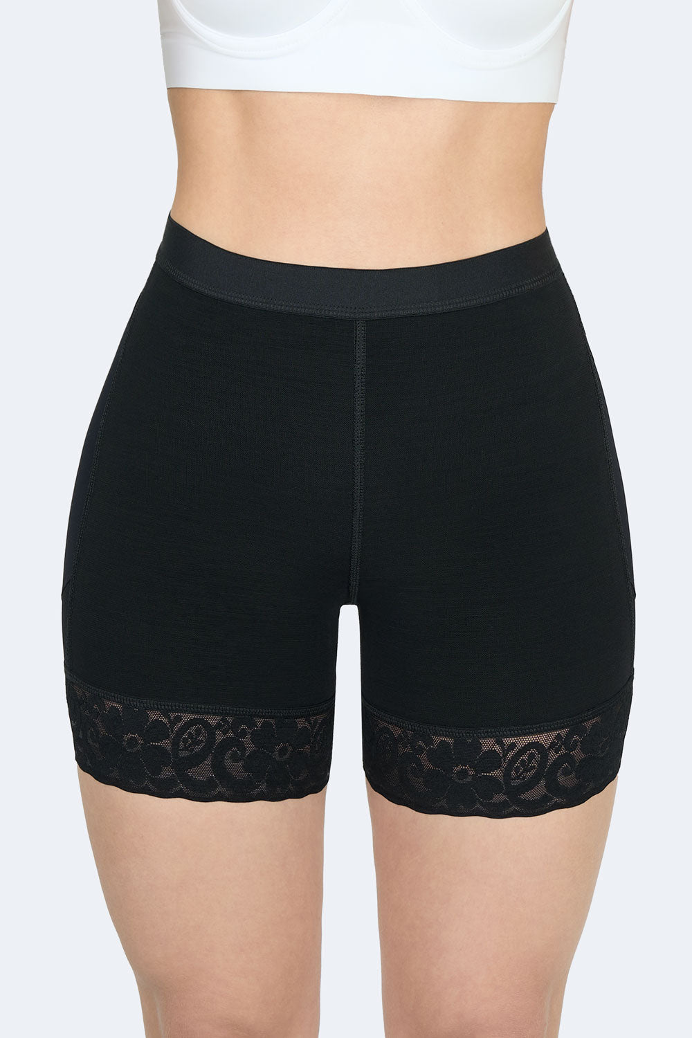 Vista frontal cercana de un short levanta cola corto en color negro, Faja Colombiana con encaje floral en los muslos que moldea abdomen y realza la figura.