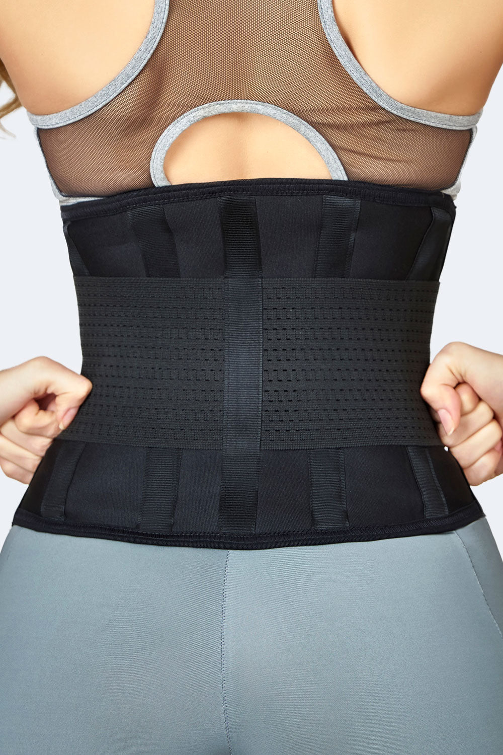 Vista posterior de mujer usando cinturon elastico negro, faja colombiana deportiva para soporte lumbar y compresion abdominal.